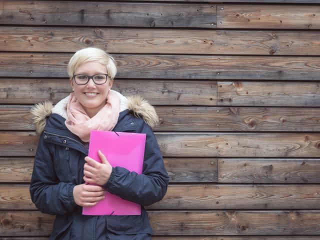 Jeune femme tenant une pochette et appuyée contre un mur.