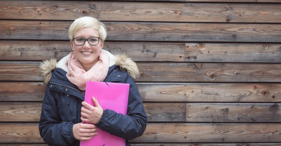 Jeune femme tenant une pochette et appuyée contre un mur.